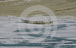 Abandoned boat sits alone on a frozen lake, untouched and desolate