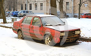 Abandoned broken-down red car in a snow-covered courtyard of an apartment building