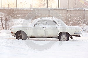 Abandoned car covered with snow in winter at sunset, warm tones, side view. Rusting, recycling, metal processing, write