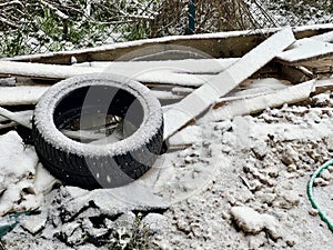 Abandoned Car Tire and Discarded Wood Under Winter\'s First Snow, Environmental Waste Concept