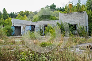 Abandoned dilapidated old brick building, broken glass from wooden frames, with ground overgrown with grass