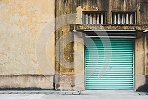 Abandoned factory building, old yellow storage warehouse building with closed green metal roller shutter door