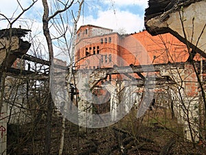 Abandoned factory complex with red brick structure framed by crumbling walls and bare trees photo