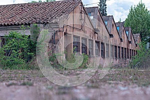 Abandoned factory with sawtooth-shaped roofs and barred windows.