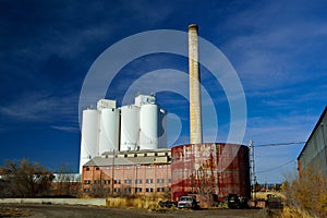 Abandoned Factory with Storage Tanks, Smokestack, and an Agriculture Grain Elevator Silo in the Background