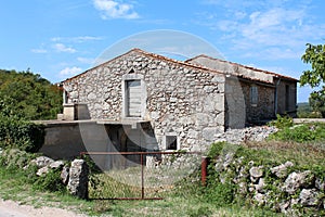 Abandoned family house built in traditional stone style with wooden window blinds and wooden doors surrounded with uncut grass and