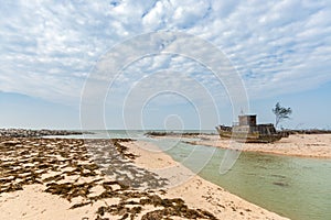 An Abandoned Fishing Boat on a beach with dry algae. At Weizhou Island, Guangxi, China.