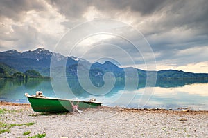 Abandoned fishing paddle boat on bank of Alps lake. Morning lake glowing by sunlight.