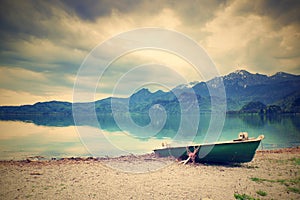 Abandoned fishing paddle boat on bank of Alps lake. Morning lake glowing by sunlight.