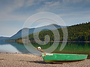 Abandoned fishing paddle boat on bank of Alps lake. Morning lake glowing by sunlight.