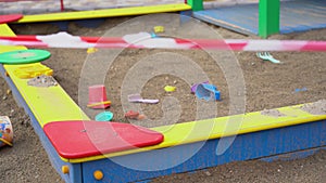 Abandoned, forgotten colored children toys buckets, scoops in closed playground close up. No entrance to sandbox during quarantine