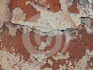 Old peeling red terracotta pink plaster on a cracked rough, scratched uneven concrete stone wall.