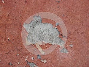 Old peeling red terracotta pink plaster on a cracked rough, scratched uneven concrete stone wall.