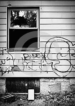 Abandoned house with broken window and graffiti.