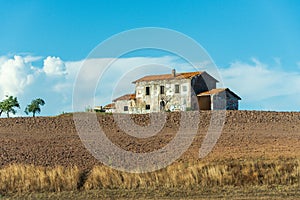 Abandoned house on the hill. Brick building covered with red tiles, broken windows and doors. Around the plowed field