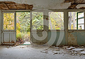 Abandoned house interior with broken glass and fallen plaster, view on overgrown autumn garden