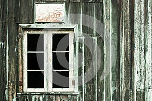 Abandoned house with old peeling grey and green wooden wall and grunge broken white window without glasses