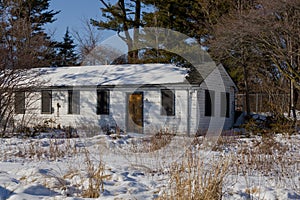 Abandoned house - windows blocked, electricity wires cut, snow covered field with trees in the background. Spring, sunny day.