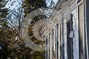 Abandoned house - windows blocked, electricity wires cut, snow covered field with trees in the background. Spring, sunny day.