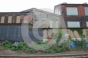 Abandoned Manufacturing Buildings With Painted Layers and Boarded Up Windows Behind Train Tracks With Cloudy Sky