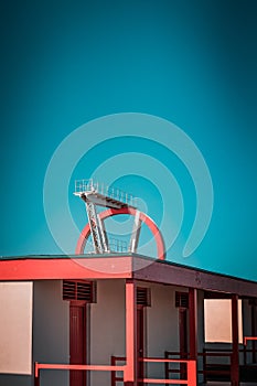 Abandoned metal diving structure. Iconic industrial and sports architecture, white and red steel elements on a deep blue clear sky