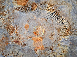 Abandoned mine tailings with helipad and colorful rusty spots over grey rough surface, view from above