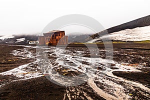 Abandoned norwegian whale hunter station rusty blubber tanks with muddy river in the foreground at Deception island, Antarctic