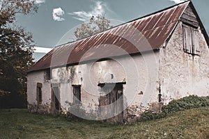 Abandoned old barn with wooden fence and grass on backyard, filtered. Weathered exterior of ancient building in village, toned.