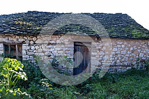 Abandoned old stonewall building aged closed wooden door, window stone roof with moss, Epirus Greece