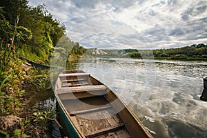 abandoned old wooden fishing boat near pier in summer lake or river. beautiful summer sunny day or evening