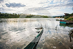 abandoned old wooden fishing boat near pier in summer lake or river. beautiful summer sunny day or evening