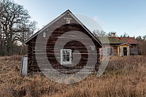 Abandoned old worn and weathered boarded wooden timber cottage house on grassy field.