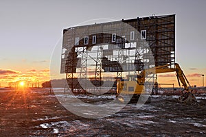 Abandoned outdoor drive in movie theater at sunset with excavator ready for demolition