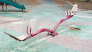 Abandoned red teeter totter and slides at a children`s outdoor playground