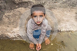 Abandoned refugee boy drinking water from river and clothes are dirty and his eyes are full of pain