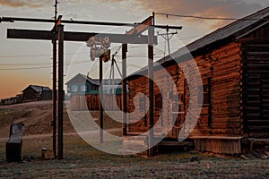 Abandoned russian village. Courtyard of old wooden house, barn with closed shutters in red warm light of sun, with shadows