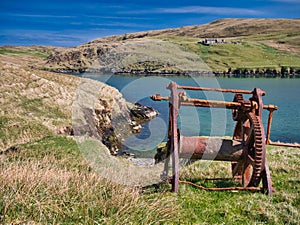 An abandoned, rusting boat winch with beach below in Shetland, UK