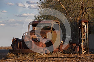 Abandoned rusty old pick up truck wreck sits derelict on the side of a road on sunset