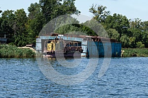 Abandoned rusty ship on the river bank. Destroyed boat and pier