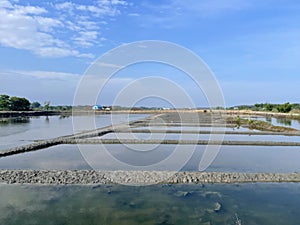 Abandoned salt ponds submerged in water with a backdrop of hills and blue sky