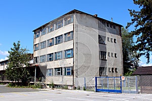 Abandoned small office building with cracked dilapidated facade and partially boarded windows surrounded with paved parking lot