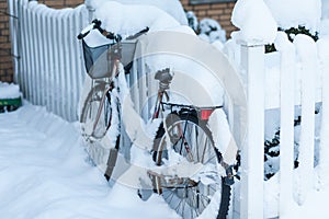 Abandoned with snow covered bike leaned at a fence in front of a