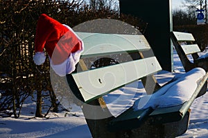Abandoned snowy park bench with Santa hat for Christmas spirit.