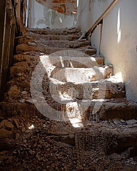 Abandoned Staircase with Ruined Carpet in Destroyed Building with Sun Shining Through Destroyed Ceiling