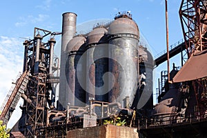 Abandoned steel mill industrial structures, rusting blast furnaces against blue skies