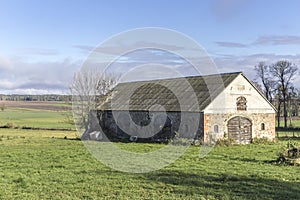 An abandoned stone barn stands in a green meadow.