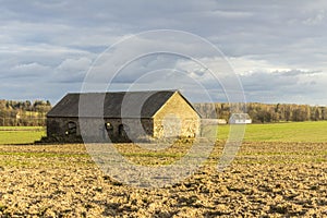An abandoned stone barn stands in the middle of a plowed field.