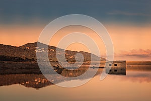 Abandoned stone building reflected in lake at sunset