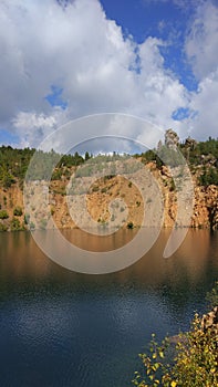 An abandoned stone quarry filled with water and trees around.