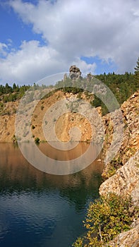 An abandoned stone quarry filled with water and trees around.